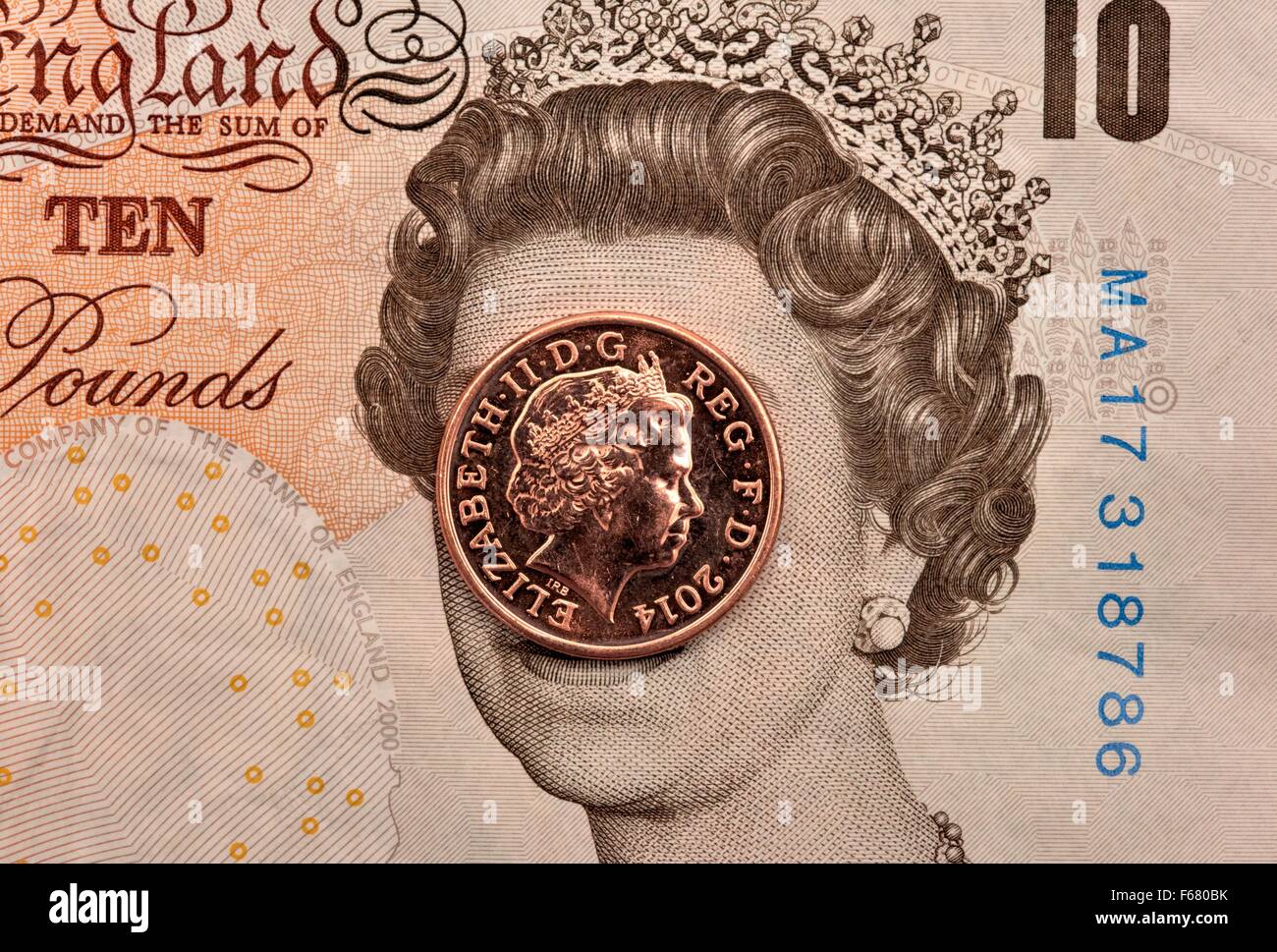 Un dieci pound nota con un penny coin che copre il Queens Head. Foto Stock