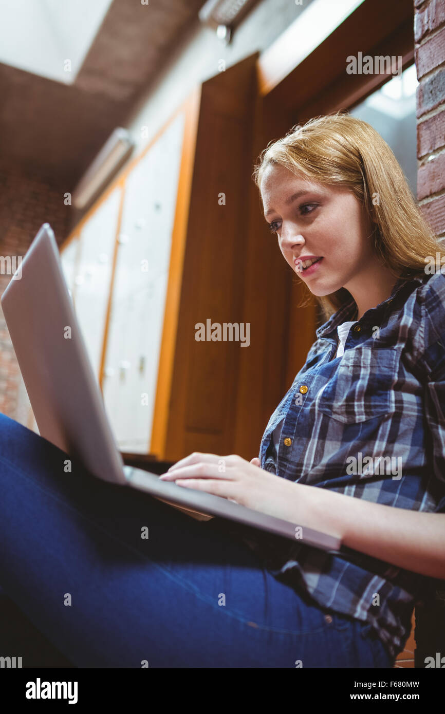 Focalizzato studente seduto sul pavimento contro il muro utilizzando laptop Foto Stock