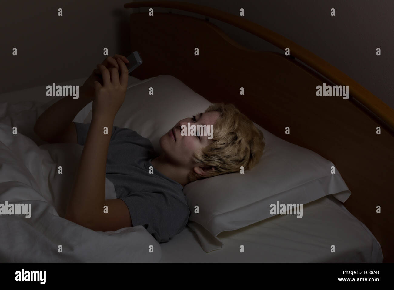 Ragazza con il suo telefono cellulare mentre nel letto. Teen utilizzando la tecnologia a tarda notte invece di dormire. Foto Stock