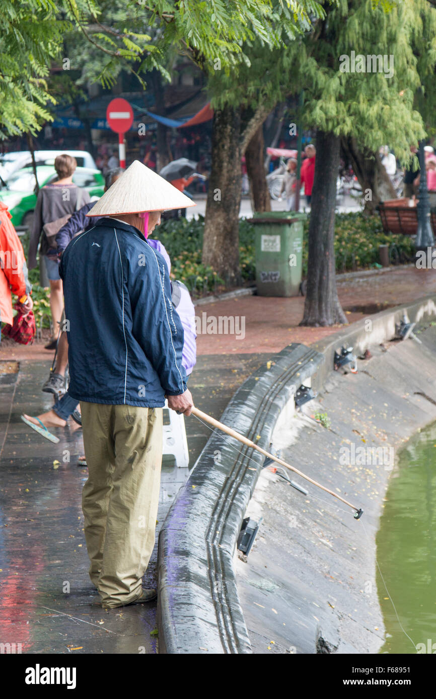 Uomo vietnamita la pesca al perimetro del lago Hoan Kiem ad Hanoi, capitale del Vietnam Foto Stock