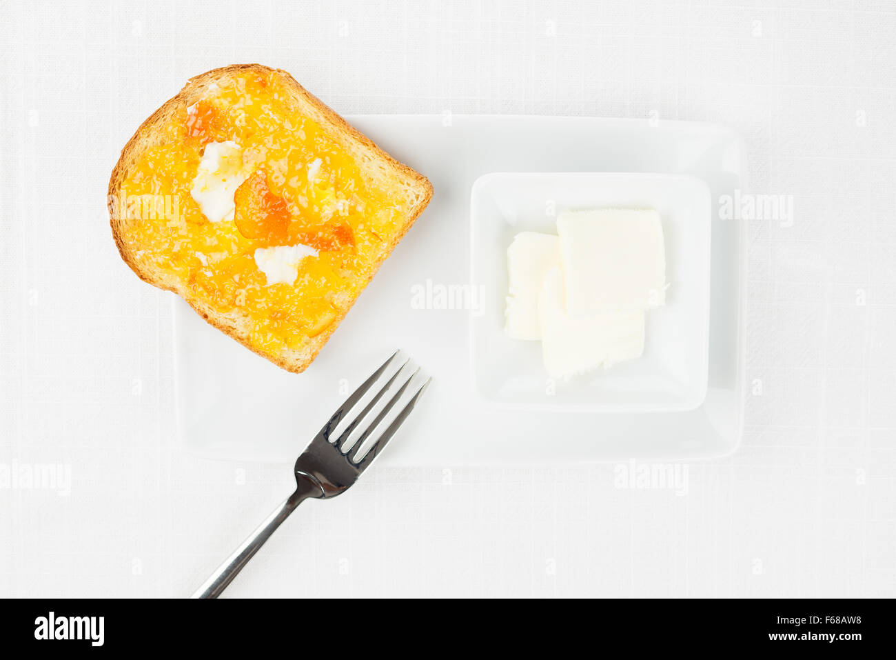 Toast alla francese con diffusione di arancia amara marmellata o confettura con frutta candita, riccioli di burro, forcella e stoviglie sulla tovaglia bianca Foto Stock