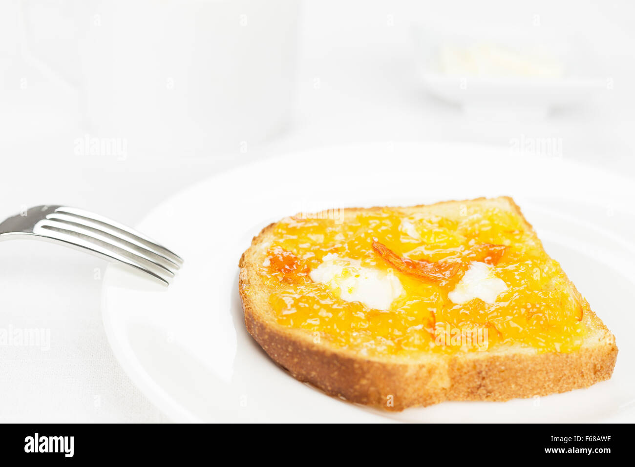 La prima colazione. Toast alla francese con diffusione di arancia amara marmellata o confettura con frutta candita, riccioli di burro, forcella sullo sfondo e una tazza Foto Stock