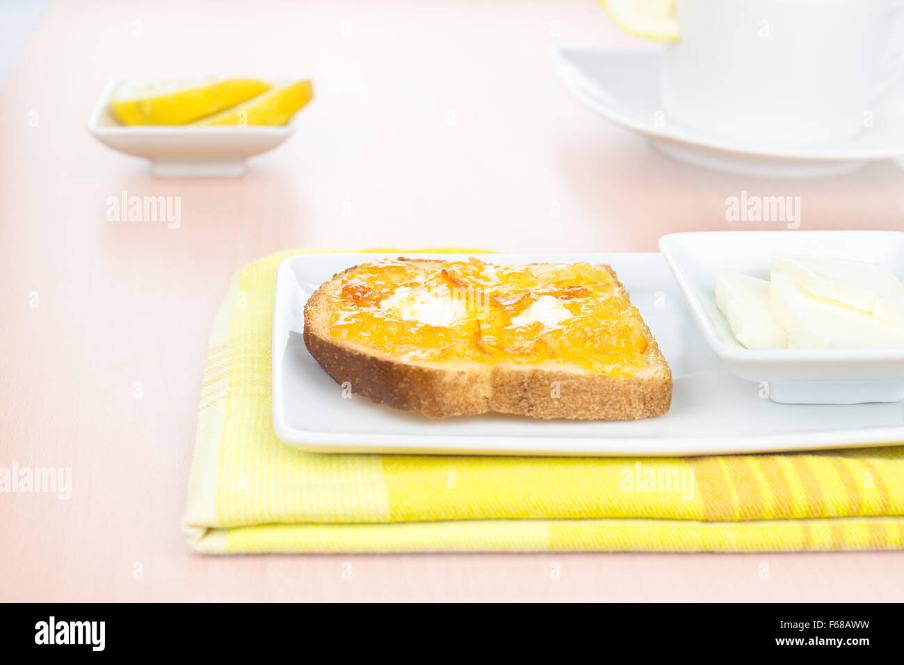 La prima colazione. Toast alla francese con diffusione di arancia amara marmellata o confettura con frutta candita, riccioli di burro, limone, una tazza e stoviglie su Foto Stock