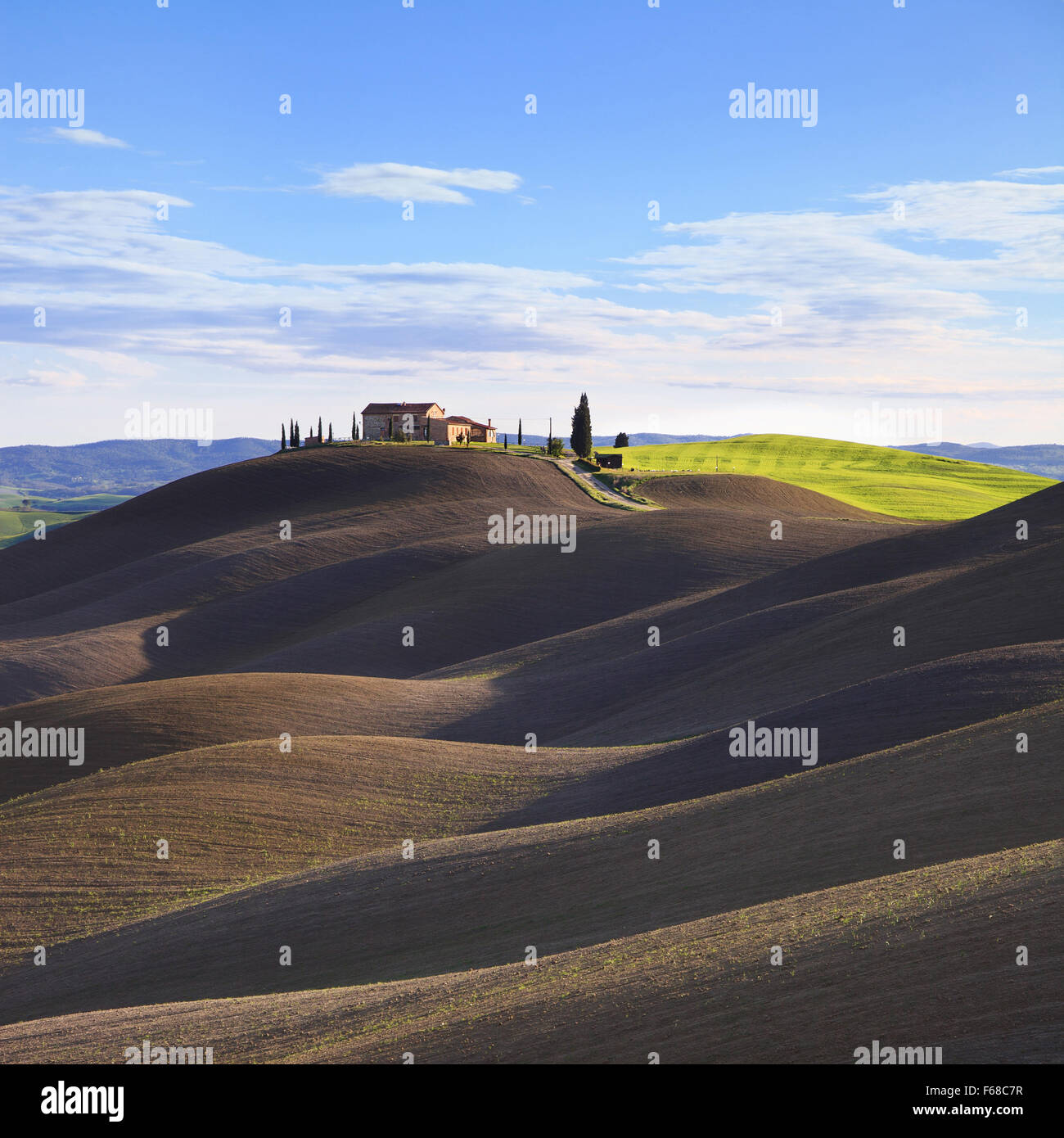 Toscana, paesaggio rurale nelle Crete Senesi a terra. Arò colline, campagna agriturismo, cipressi secolari, campo verde e blu cielo Foto Stock