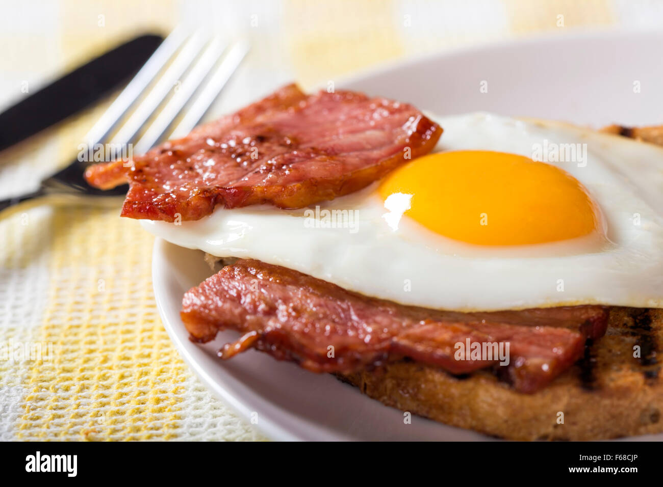 Uova e bacon con toast su una piastra bianca con coltello e forchetta Foto Stock