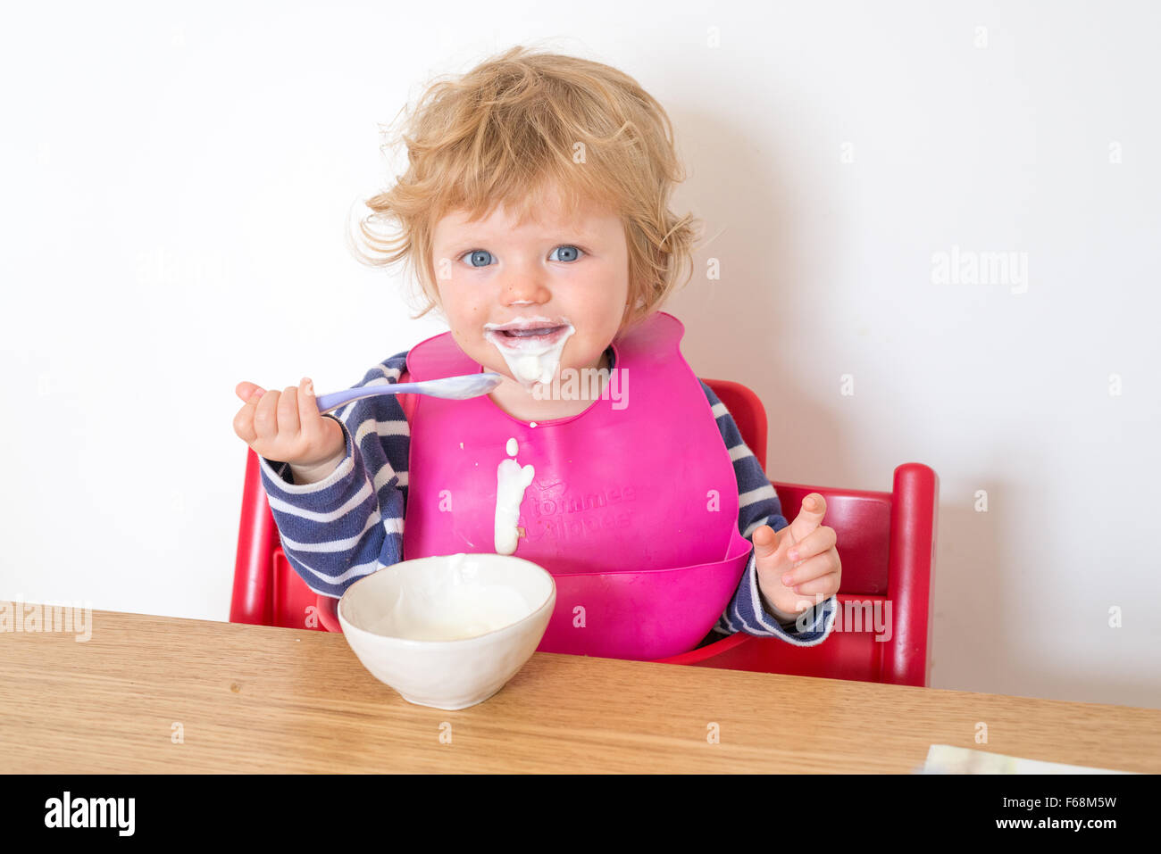 Un anno di età bambino mangiare yogurt messily, England, Regno Unito Foto Stock