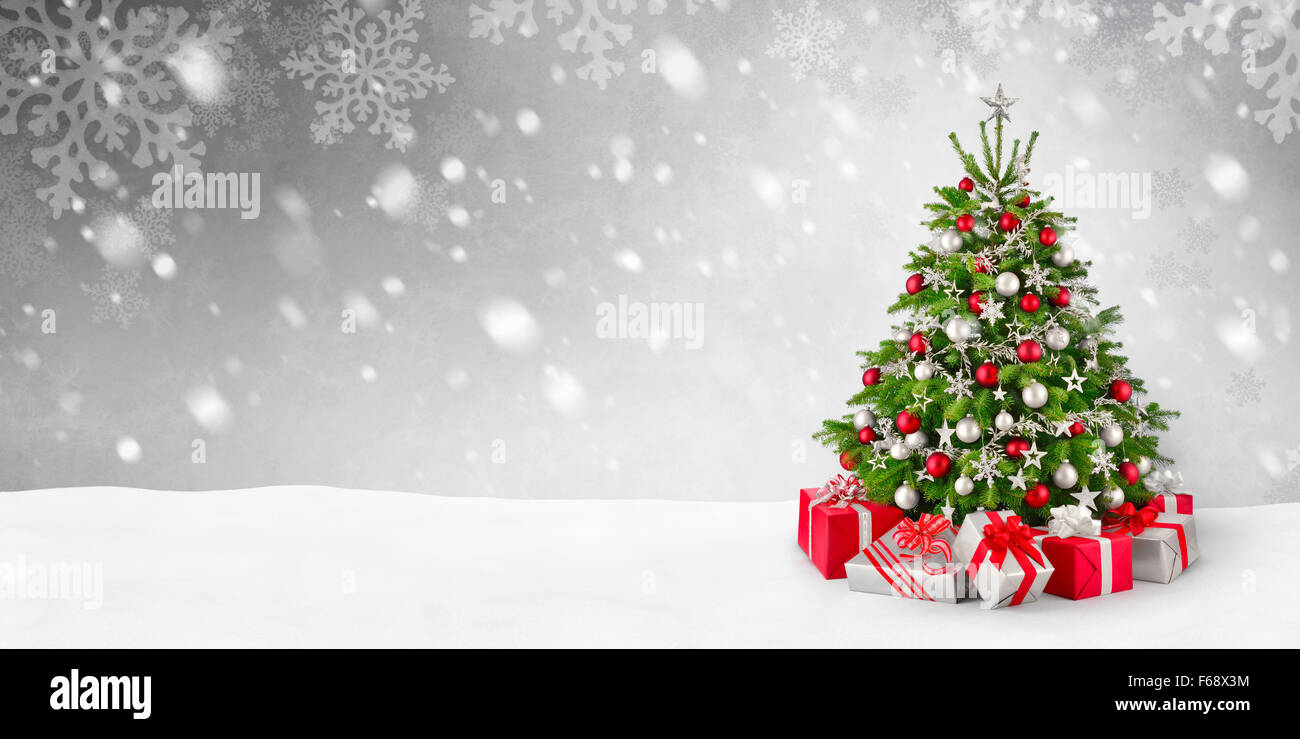 Splendida elegante albero di Natale con doni in rosso e argento su una panoramica sullo sfondo di neve Foto Stock
