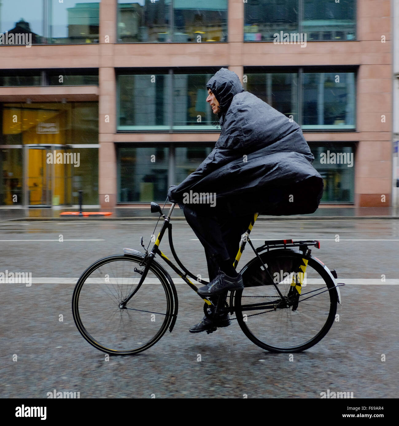 Ciclista indossando un poncho cape sotto la pioggia Foto Stock