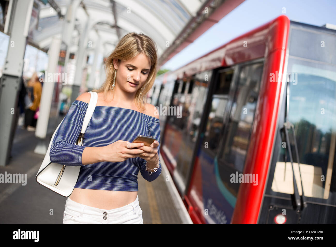 Giovane donna alla stazione ferroviaria utilizzando il suo telefono Foto Stock