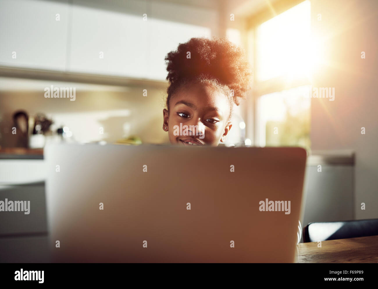 Sorridente ragazza nera con una bella acconciatura seduto a un computer portatile durante la navigazione in internet e la sua media sociali o di lavoro su h Foto Stock