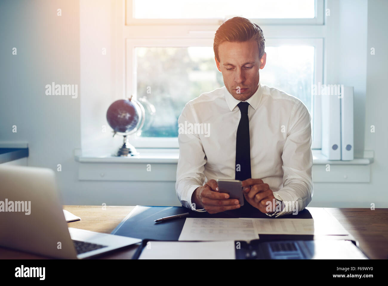 Executive business man sms sul suo telefono cellulare e controllare la posta mentre è seduto alla sua scrivania in ufficio Foto Stock