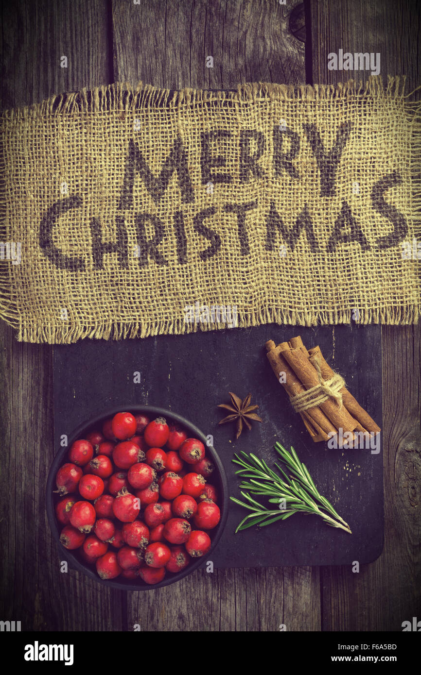 Buon Natale saluto sul materiale di lino decorato con bastoncini di cannella, anice stellato, rosmarino e bacche rosse Foto Stock