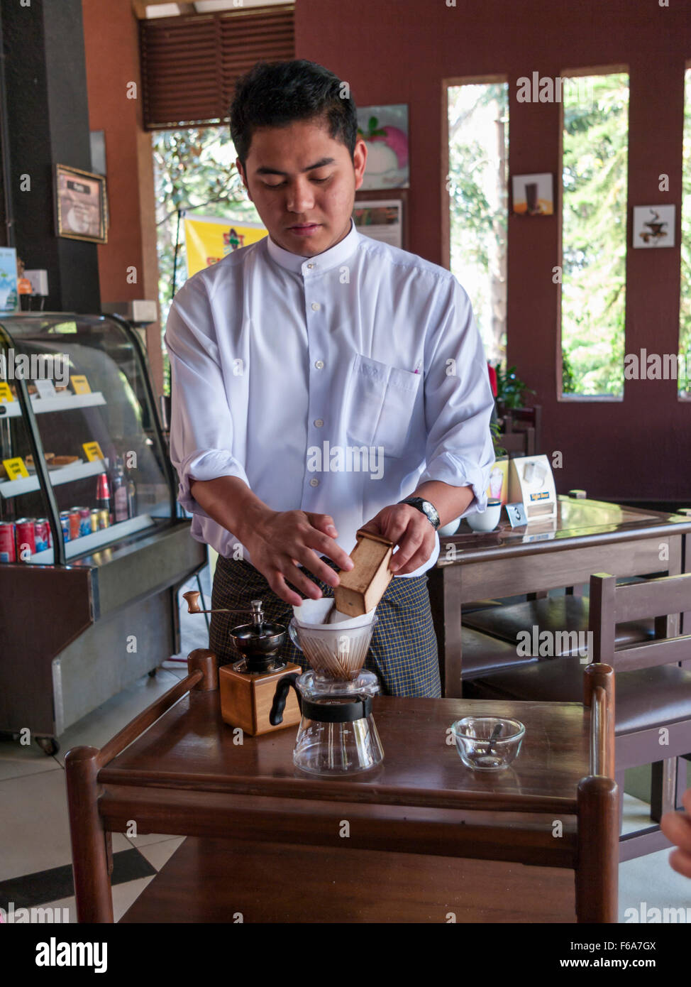 Cameriere in un caffè di Pyin Oo Lwin (Maymyo) in Myanmar la preparazione del caffè fresco, versando la massa i fagioli in un filtro. Foto Stock