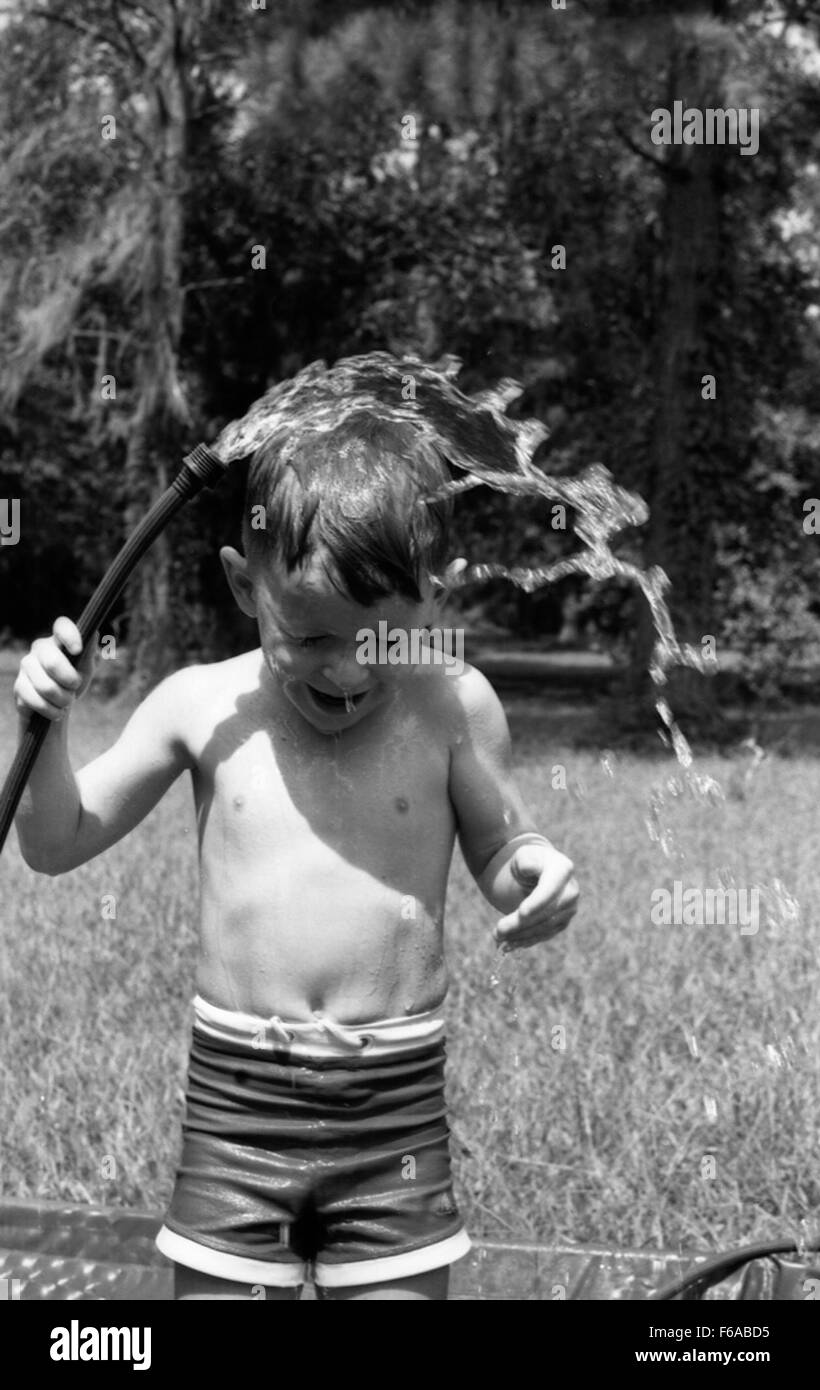 Un'istantanea di una persona che si raffredda con un tubo da giardino a Tallahassee, in Florida, durante una giornata calda. La scena riflette le tipiche attività estive, con la persona che si gode un momento rinfrescante nel caldo all'aperto, illustrando la vita quotidiana in una città della Florida. Foto Stock