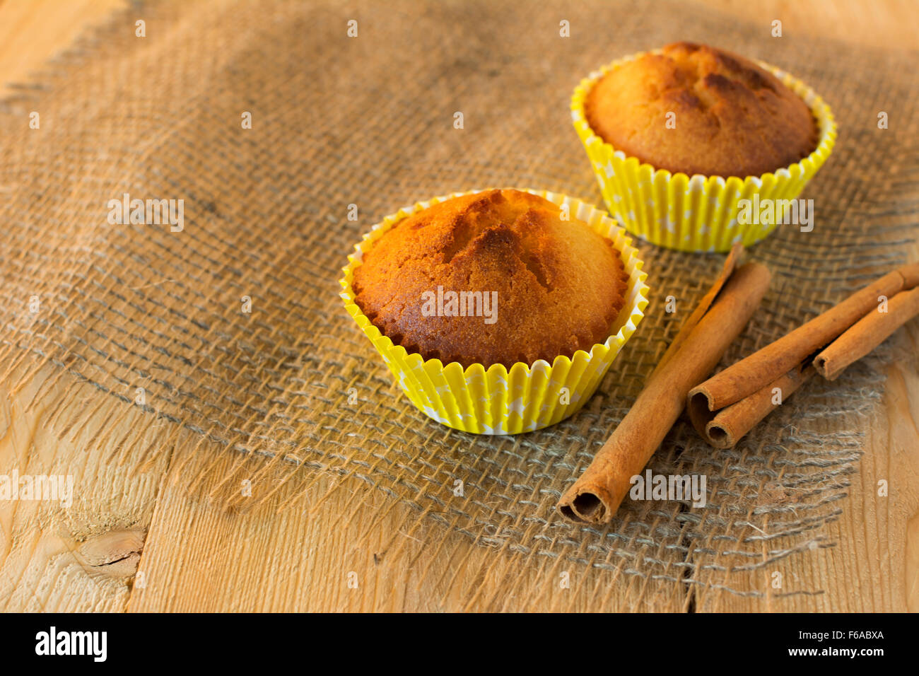 Muffin in carta gialla cupcake titolare su un letto di sacco e di bastoncini di cannella, il fuoco selettivo Foto Stock