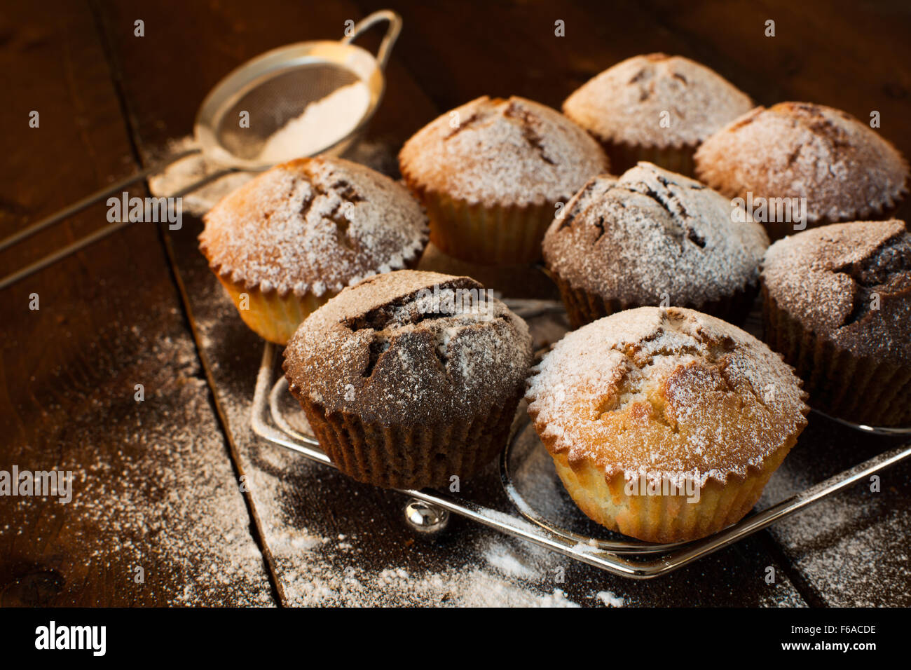 Vaniglia e cioccolato muffin su di un supporto in metallo, zucchero semolato, crivello inferiore per una cottura al buio su un sfondo di legno, fuoco selettivo Foto Stock