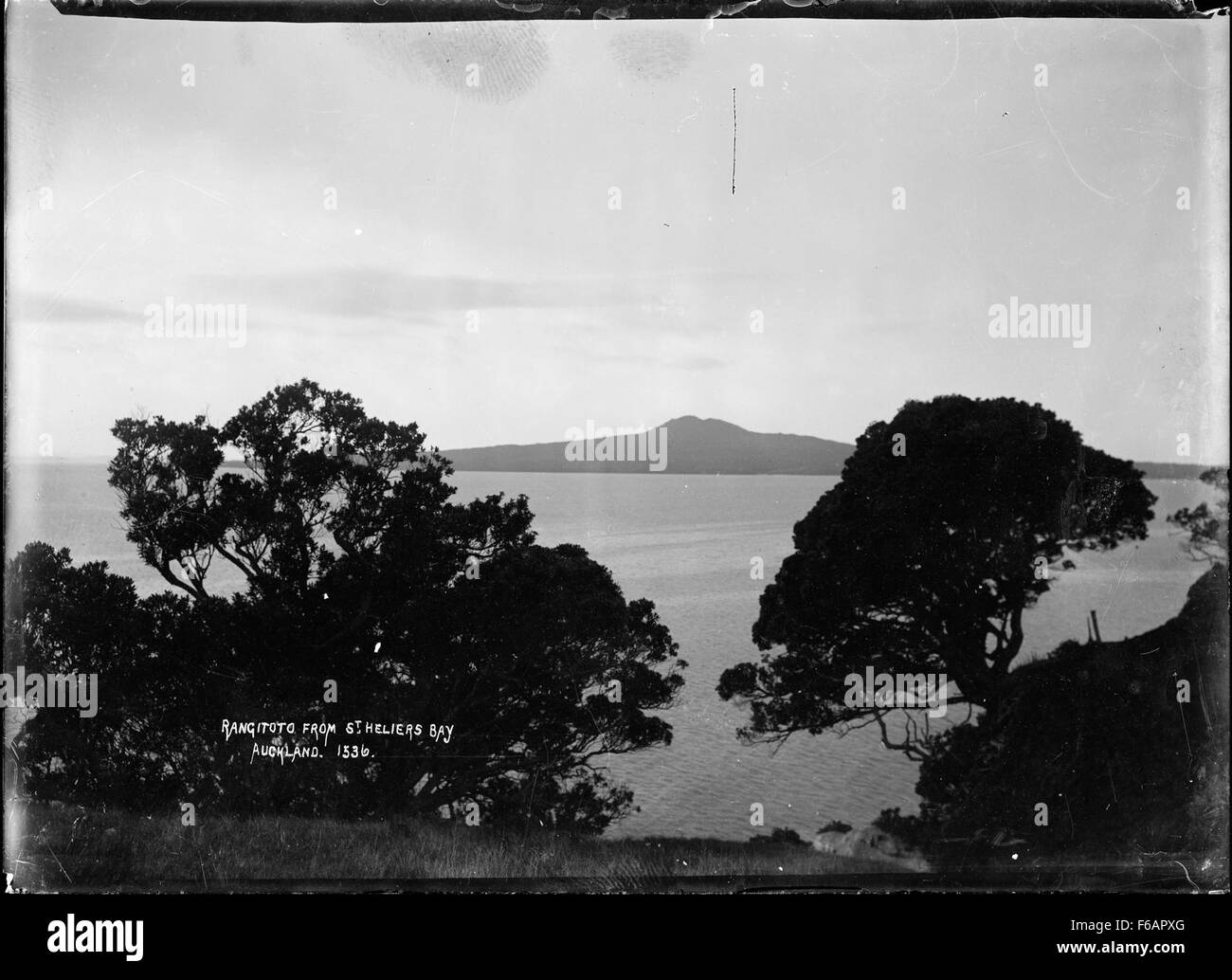 Questa fotografia cattura l'isola di Rangitoto, situata al largo della costa di Auckland, nuova Zelanda, vista dalla baia di St Heliers. La caratteristica forma vulcanica dell'isola e i lussureggianti dintorni verdi sono raffigurati contro il cielo azzurro. Foto Stock