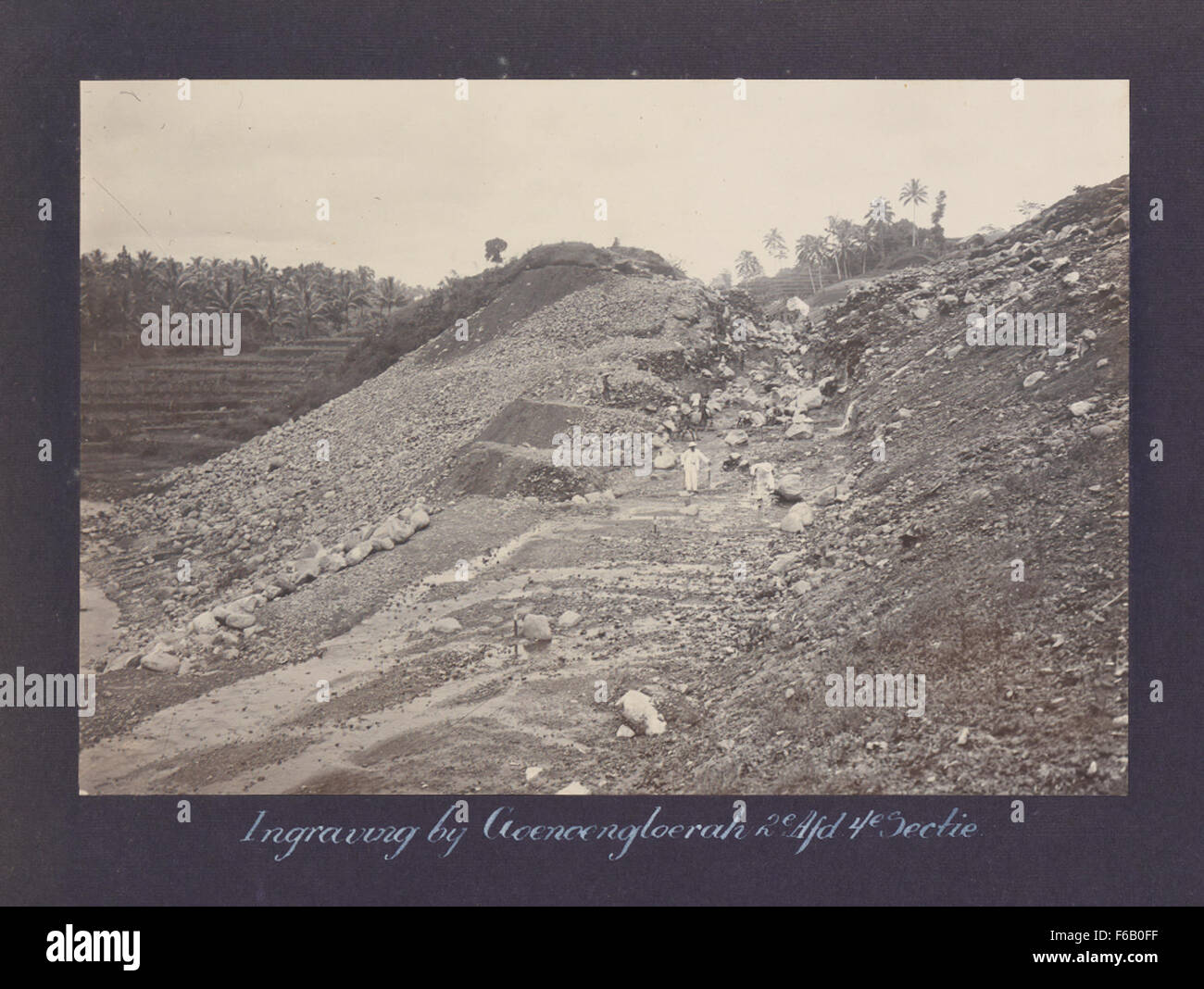 Questa incisione, intitolata 'Ingraving bij Goenoengloerah', raffigura lavoratori che costruiscono ferrovie nel secondo dipartimento, quarta sezione delle Ferrovie di Stato nei Paesi Bassi. L'immagine offre un'istantanea dello sviluppo ferroviario del XIX secolo e del lavoro coinvolto nella costruzione di infrastrutture critiche. Foto Stock