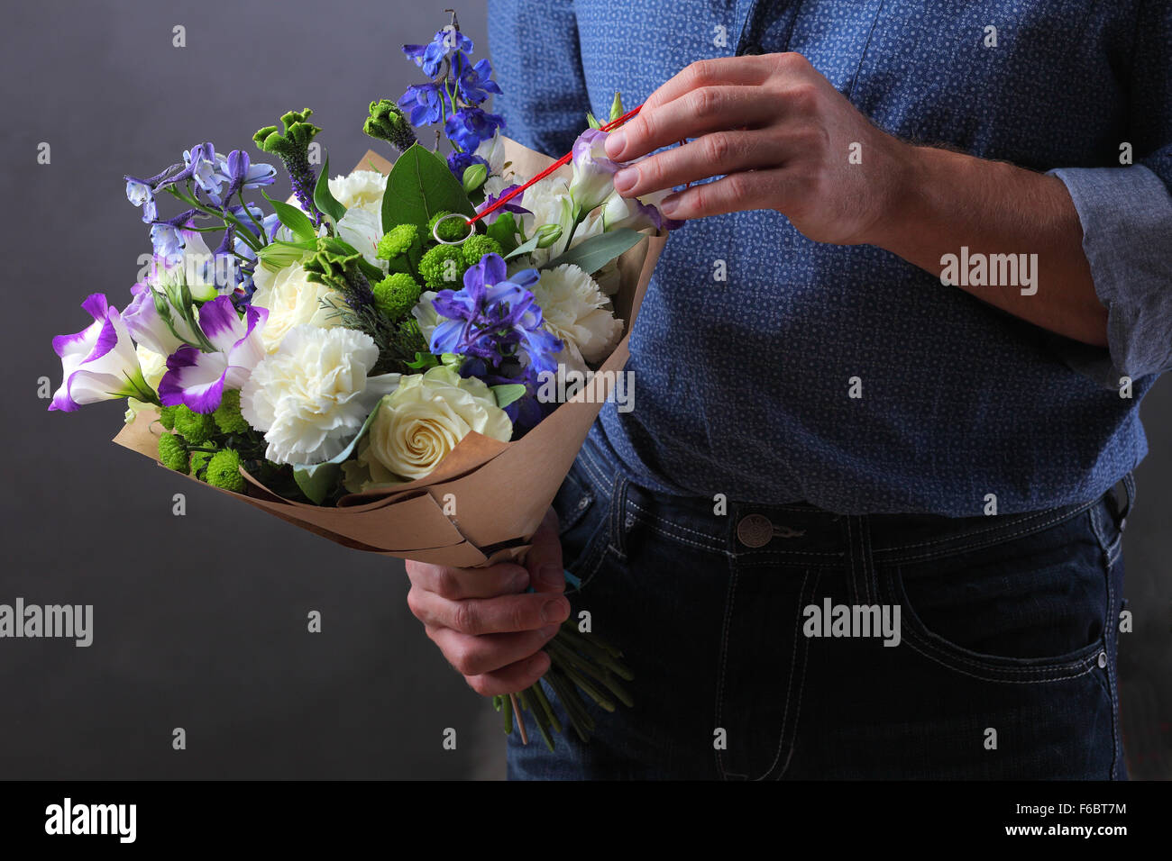 Uomo con un bouquet di fiori, un uomo fa una proposta per una donna, un amante di fiori e un anello, amore nota nascosti nei fiori, nota padrona, Foto Stock