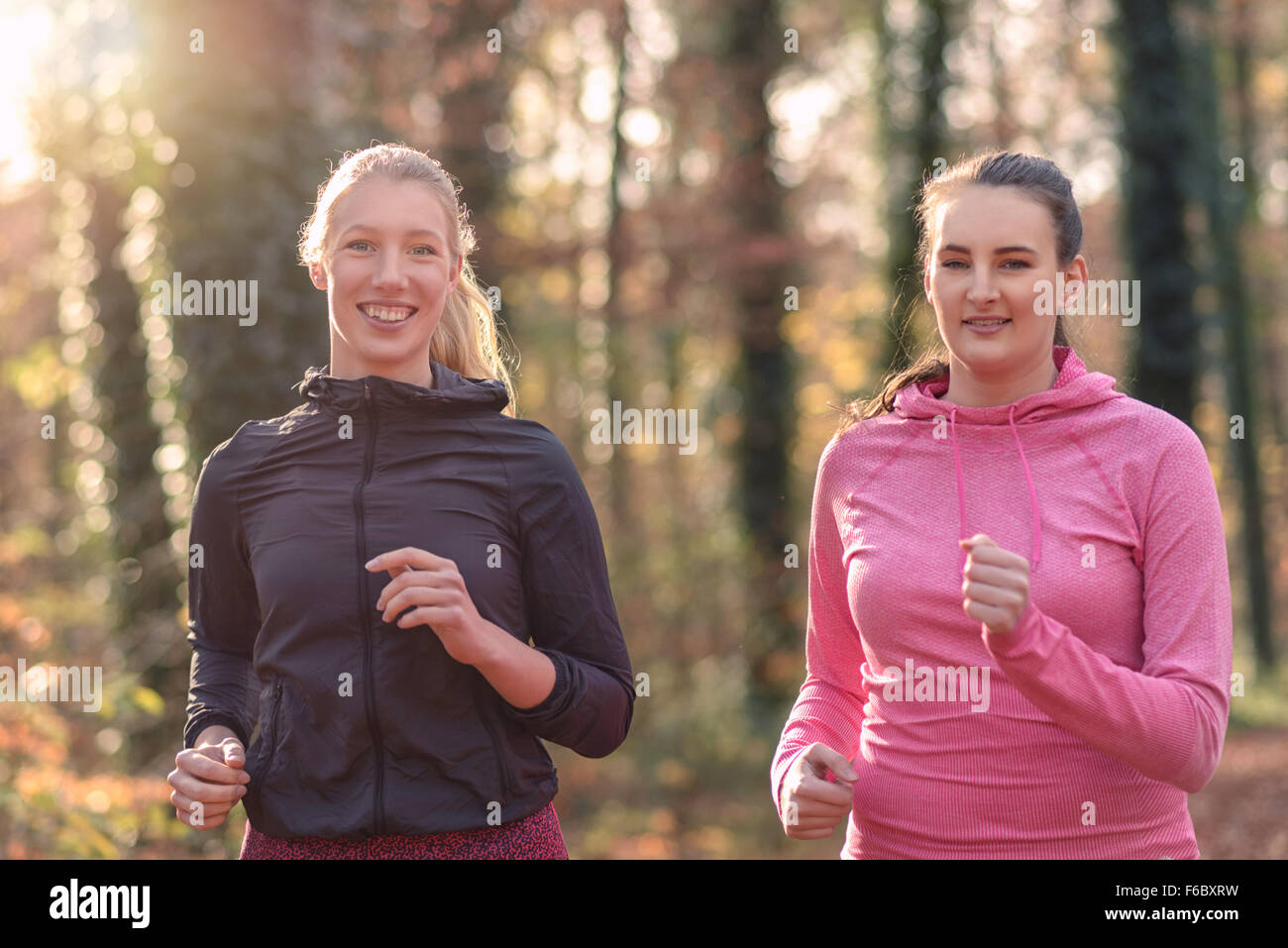 Due attraenti montare le giovani signore jogging insieme attraverso una foresta di autunno in chat come essi corrono attraverso gli alberi, in un healt Foto Stock