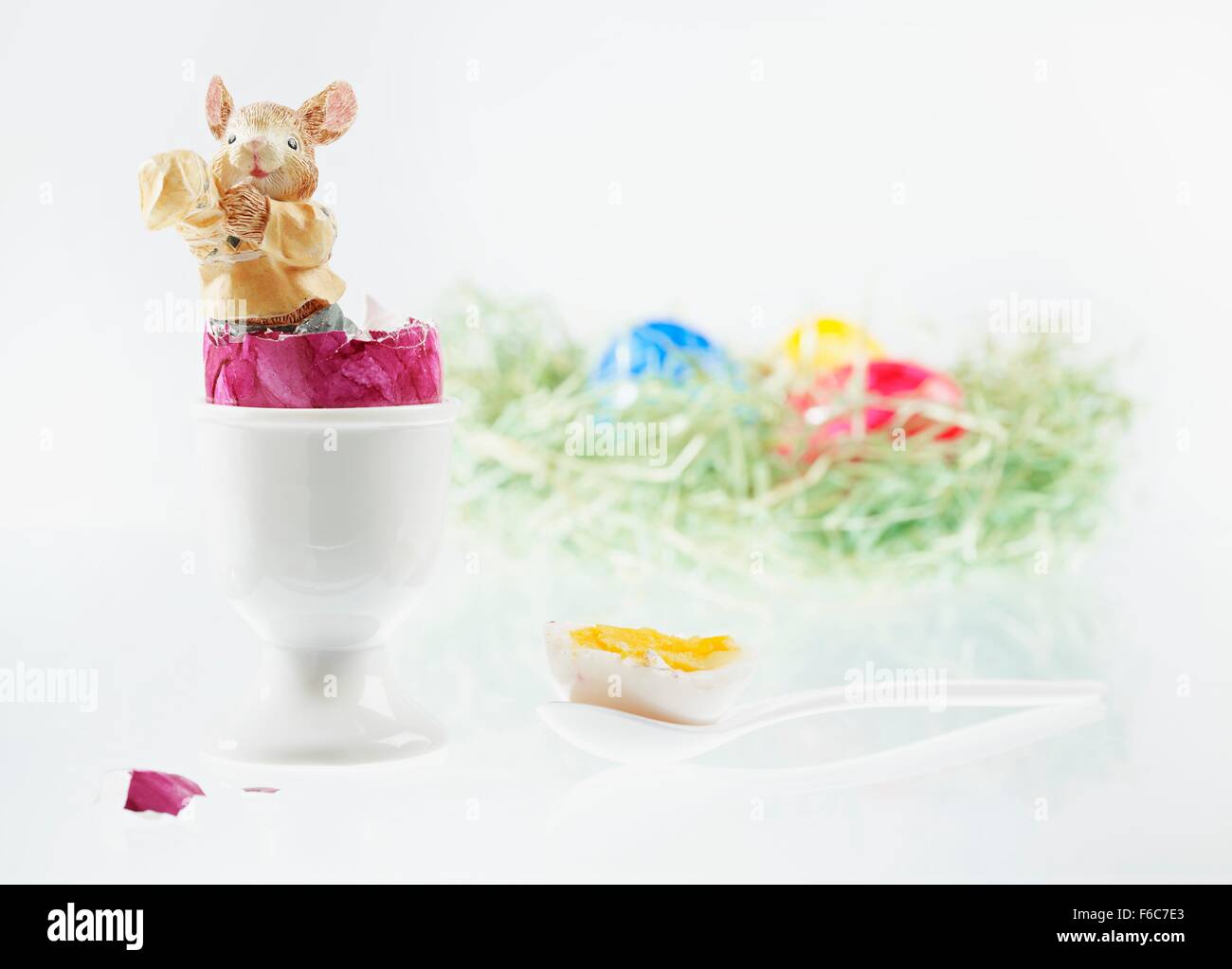 Un coniglietto di pasqua statuetta in un uovo sodo con il top cut off, con un nido di Pasqua di uova colorate in background Foto Stock