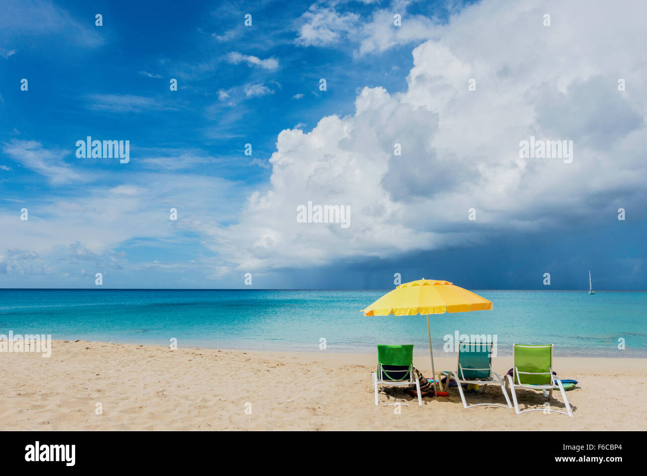 Tre sedie a sdraio sotto un ombrello giallo si affacciano su una tempesta tropicale al di sopra dei Caraibi. St Croix, U.S. Isole Vergini. Foto Stock