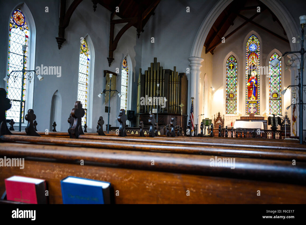 Interno di una piccola vecchia chiesa vuota con vetrate decorative, pulpito e organo a canne, legno pew e inno libri Foto Stock