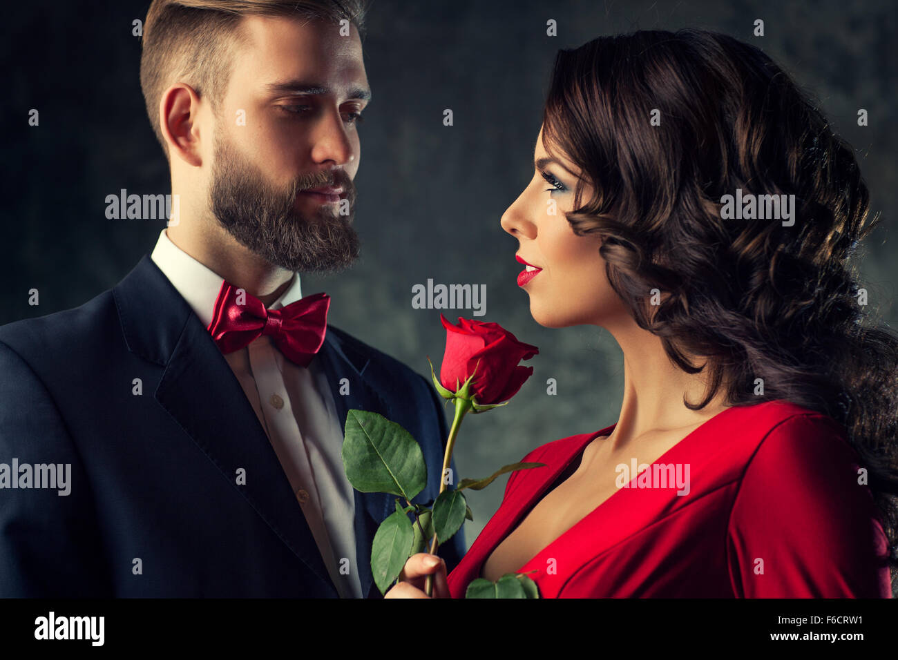 Giovane ed elegante giovane in abito da sera ritratto. Woman in Red Rose di contenimento e alla ricerca sull'uomo. Focus sulla donna. Foto Stock