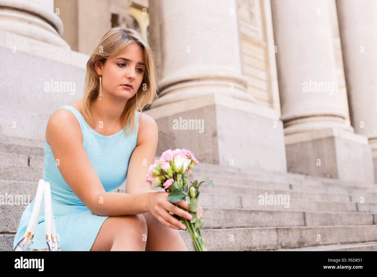 Triste ragazza seduta sui gradini tenendo un mazzo di fiori Foto Stock