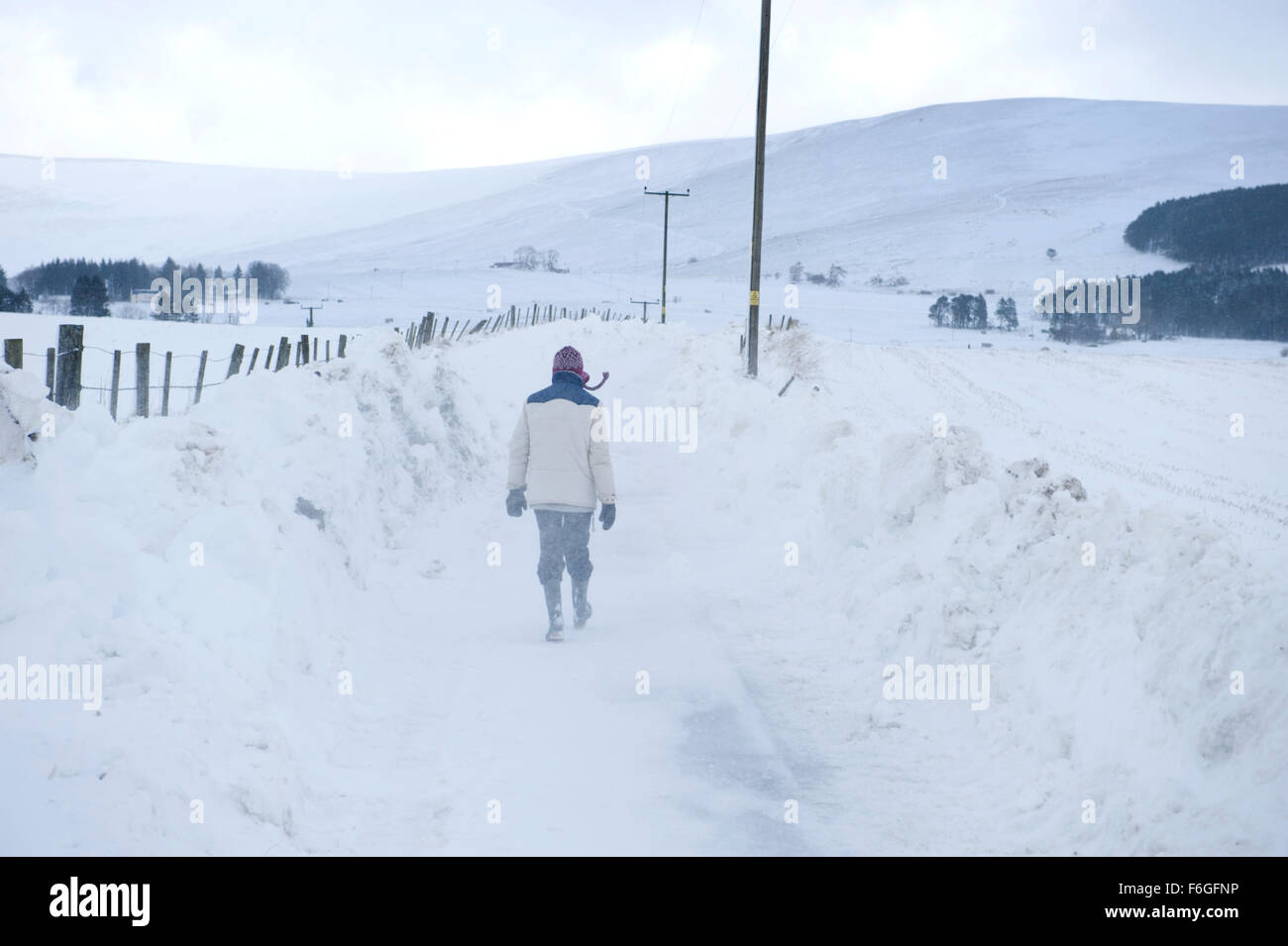 Una donna sola a fare una passeggiata in una coperta di neve remote lane in Aberdeenshire Foto Stock