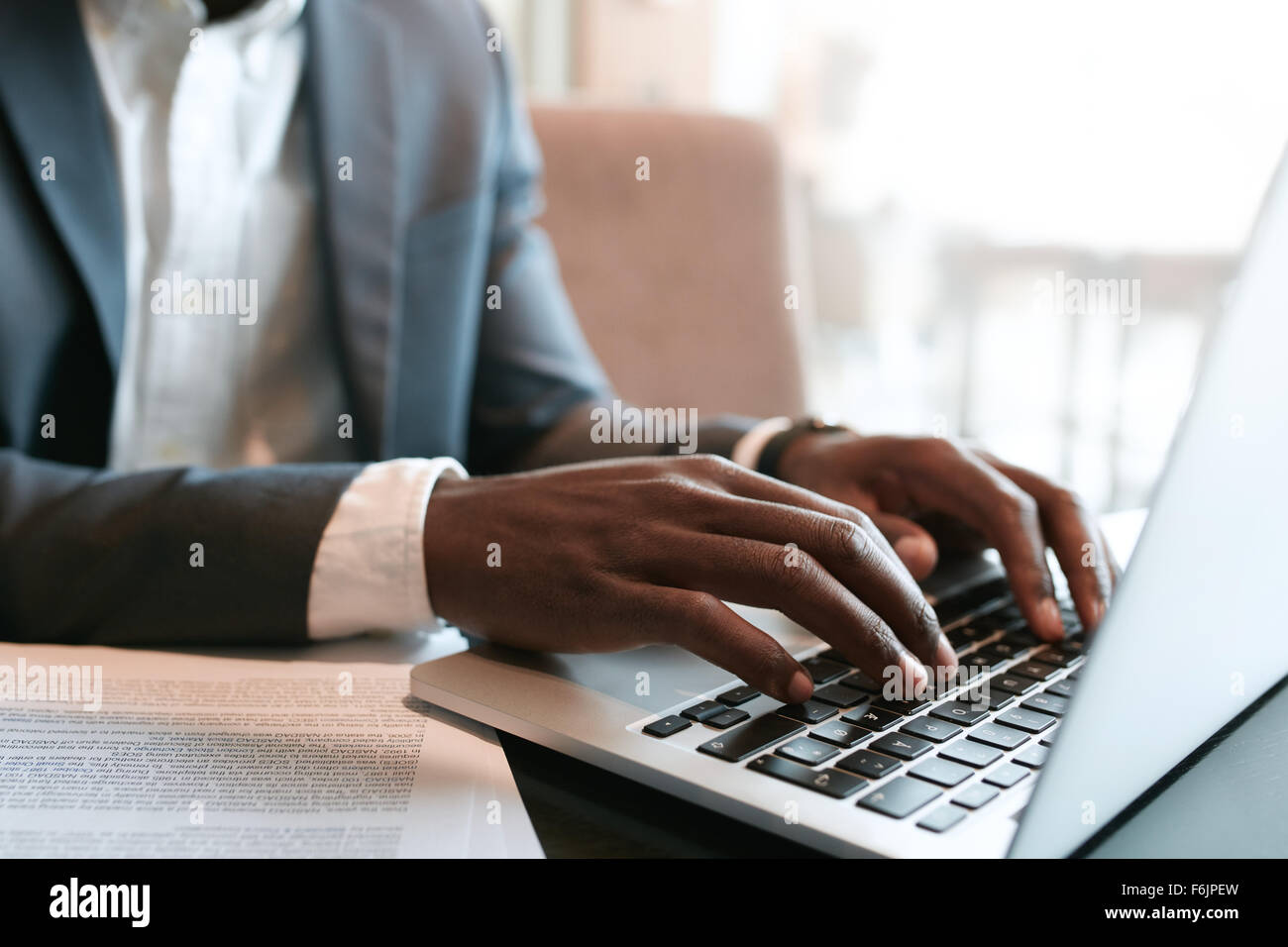 Imprenditore lavorando sul computer portatile con alcuni documenti sul tavolo. Chiudere fino a mani maschio digitando sulla tastiera del notebook. Foto Stock