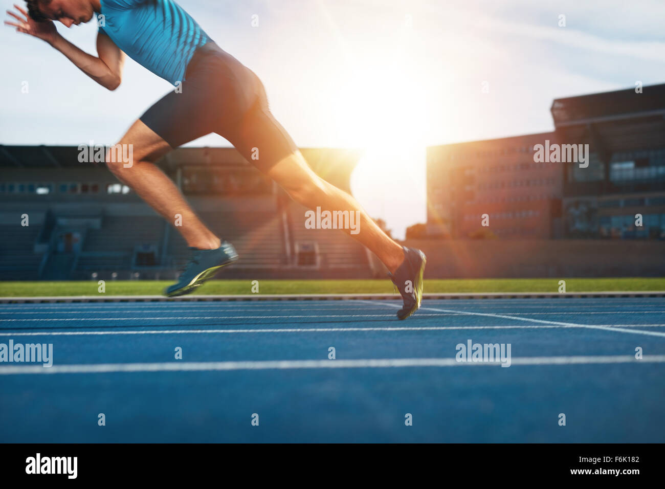 Colpo di giovane atleta maschio lanciando fuori dalla linea di partenza in una gara. Runner in esecuzione sulla pista di atletica dello stadio. Foto Stock