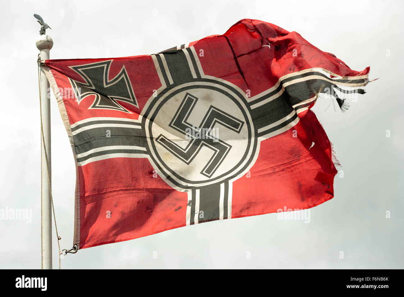 La seconda guerra mondiale la rievocazione. Lacerato dalla guerra della Wehrmacht tedesca bandiera con croce di ferro e con la svastica nazista, svolazzanti sulla sommità del pennone contro tempestoso cielo grigio. Foto Stock