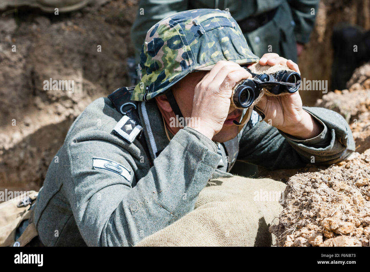 WW2 rievocazione. Il tedesco Wehrmacht Officer nascosto in trincea  guardando sopra la parte superiore attraverso il binocolo in una giornata  di sole. Indossa il casco di mimetizzazione Foto stock - Alamy