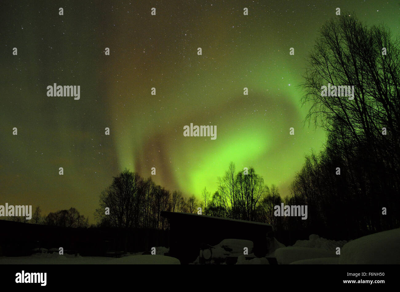 Forte verde aurora boreale su strade coperte di neve montagna e foresta invernale nel circolo polare artico Foto Stock