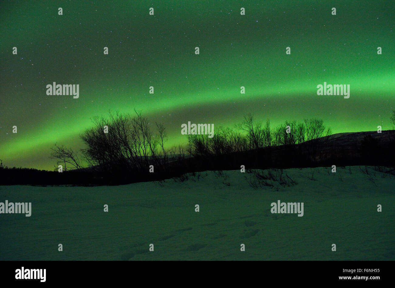 Forte verde aurora boreale su strade coperte di neve montagna e foresta invernale nel circolo polare artico Foto Stock