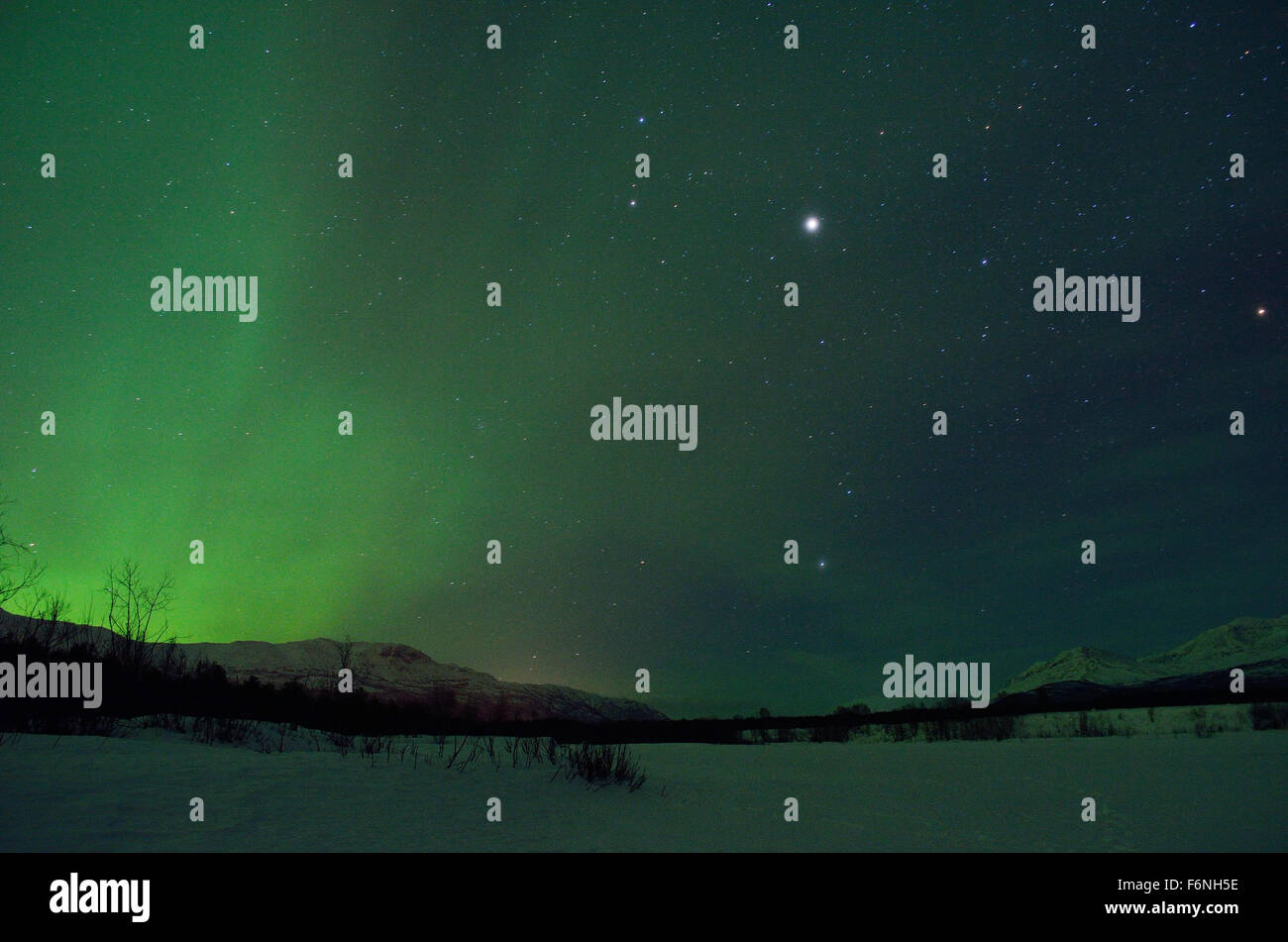 Forte verde aurora boreale su strade coperte di neve montagna e foresta invernale nel circolo polare artico Foto Stock