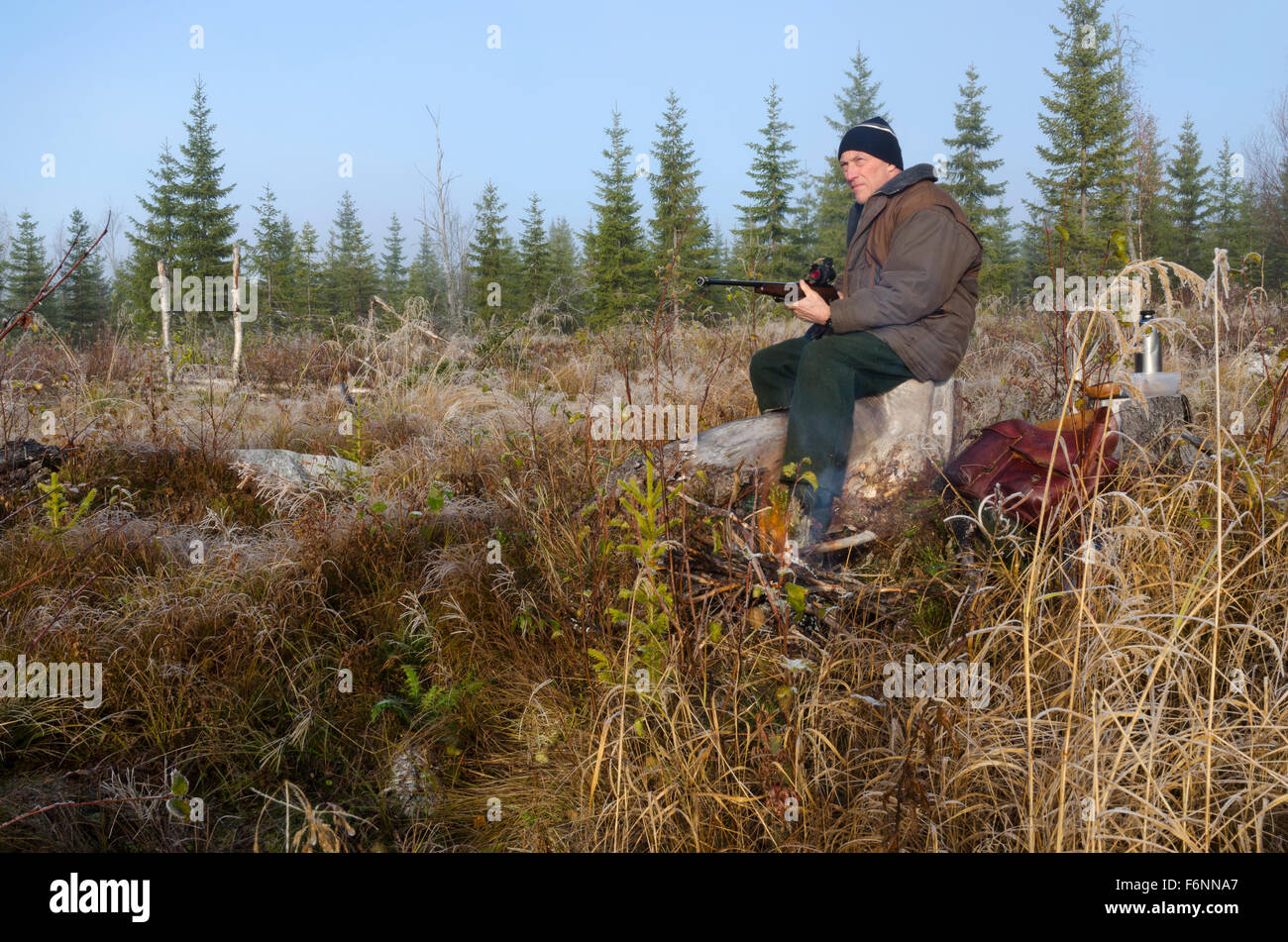 Moose hunter seduti su un moncone con un po' fuoco davanti tenendo il suo fucile rivolta in avanti, immagine dal nord della Svezia. Foto Stock