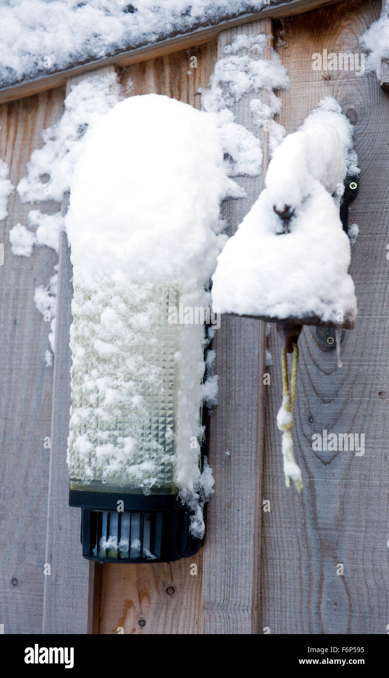 Accumulo di neve e ghiaccio su un vecchio campanello e un più moderno luminoso esterno Foto Stock