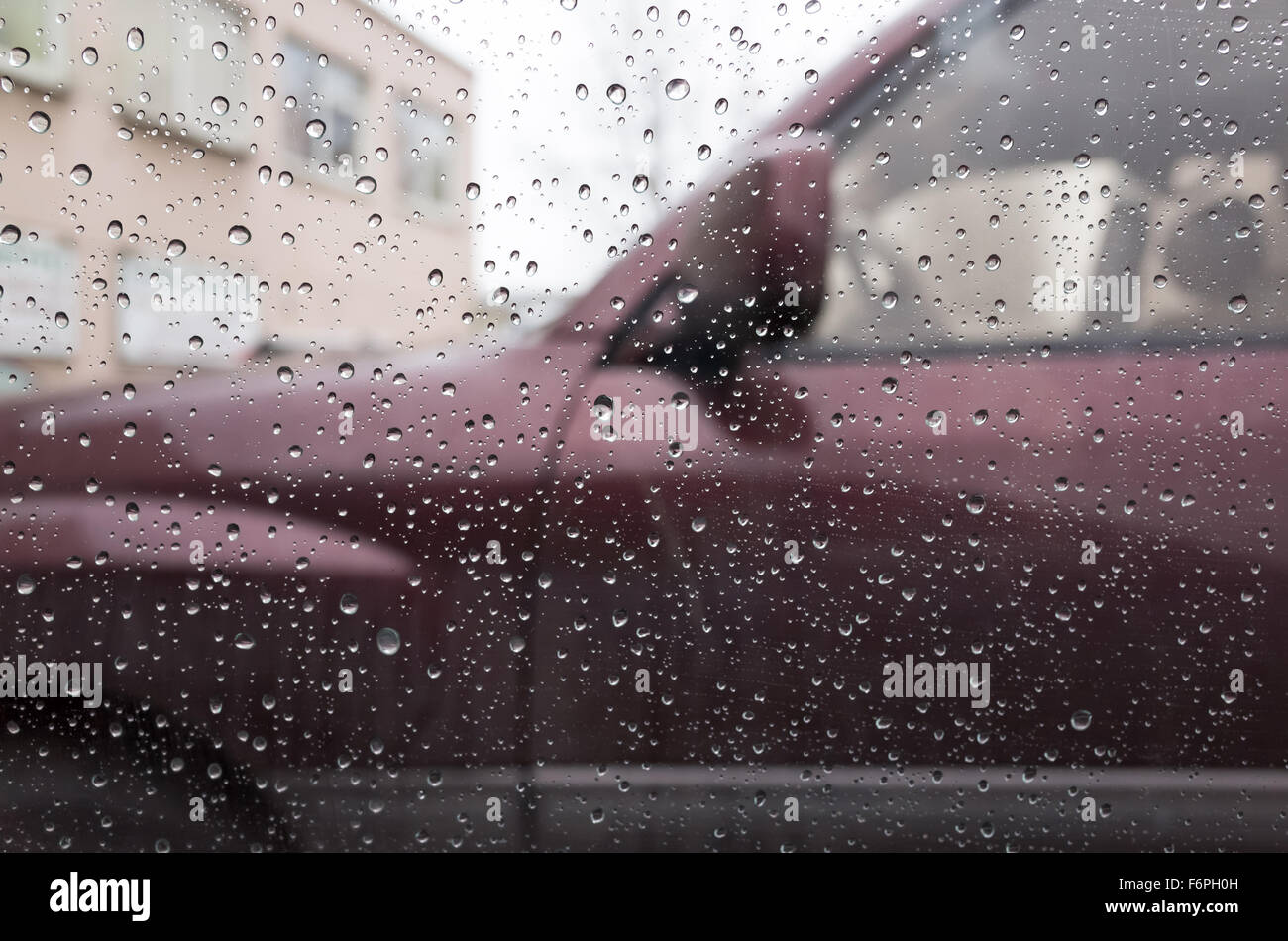 Wet finestra auto con gocce di pioggia e una vettura sfocata dietro. Primo piano con messa a fuoco selettiva e DOF poco profondo Foto Stock