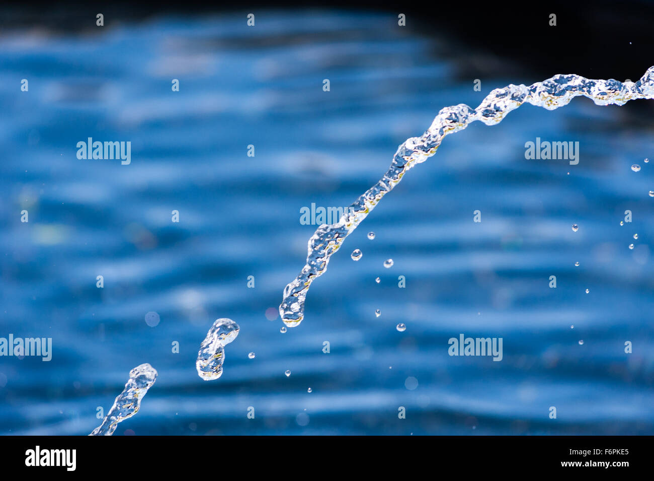 Abstract close-up illuminato del flusso di acqua e gocce che cadono in arco contro sfocato sfondo blu. Foto Stock