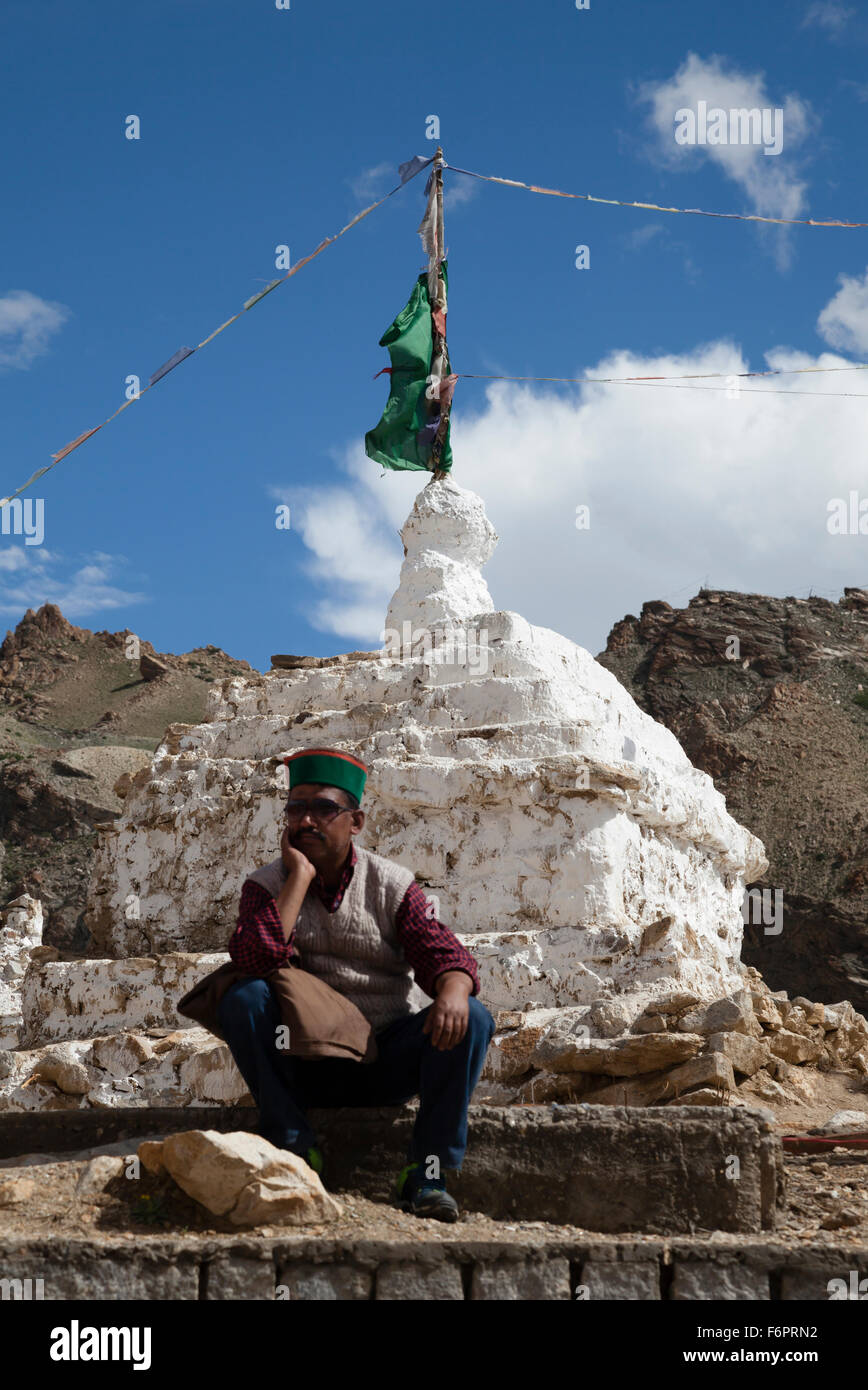 Indian uomo in abito tradizionale seduta accanto alla stupa buddisti nella regione himalayana di Himachal Pradesh Foto Stock