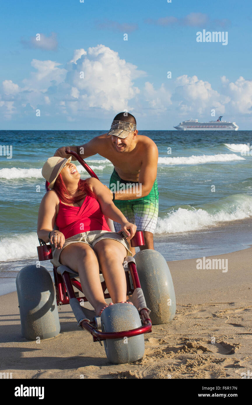 Uomo paraplegico di spinta ragazza in sedia a rotelle sulla spiaggia Foto Stock