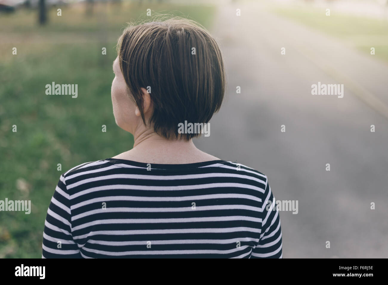 Donna informale da dietro a piedi giù per la strada vuota sul pomeriggio autunnale, dai toni rétro immagine con il fuoco selettivo Foto Stock