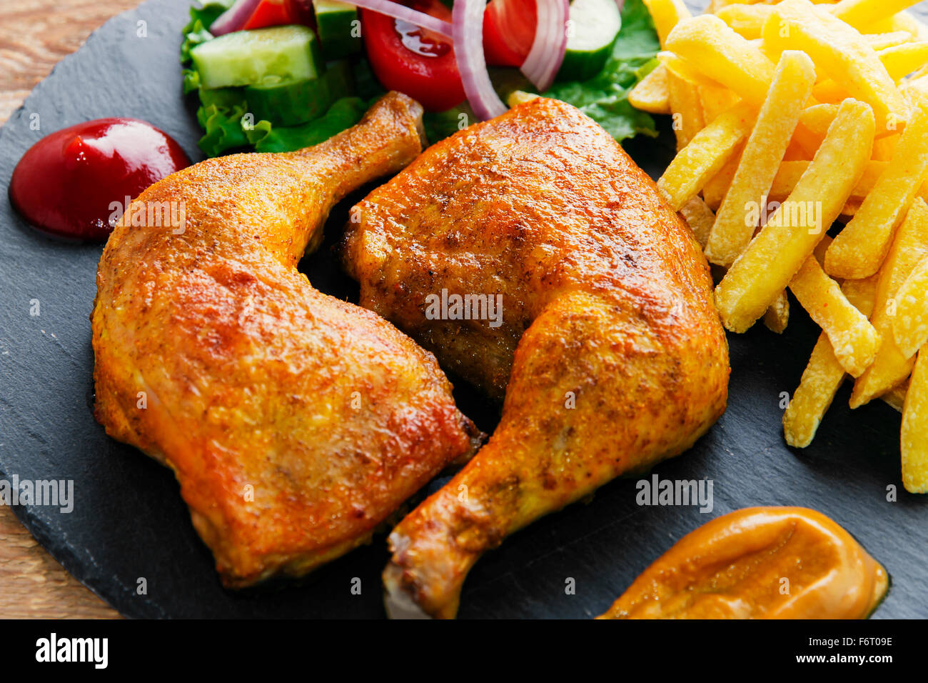 Arrosto di cosce di pollo con patatine fritte e insalata mista Foto Stock