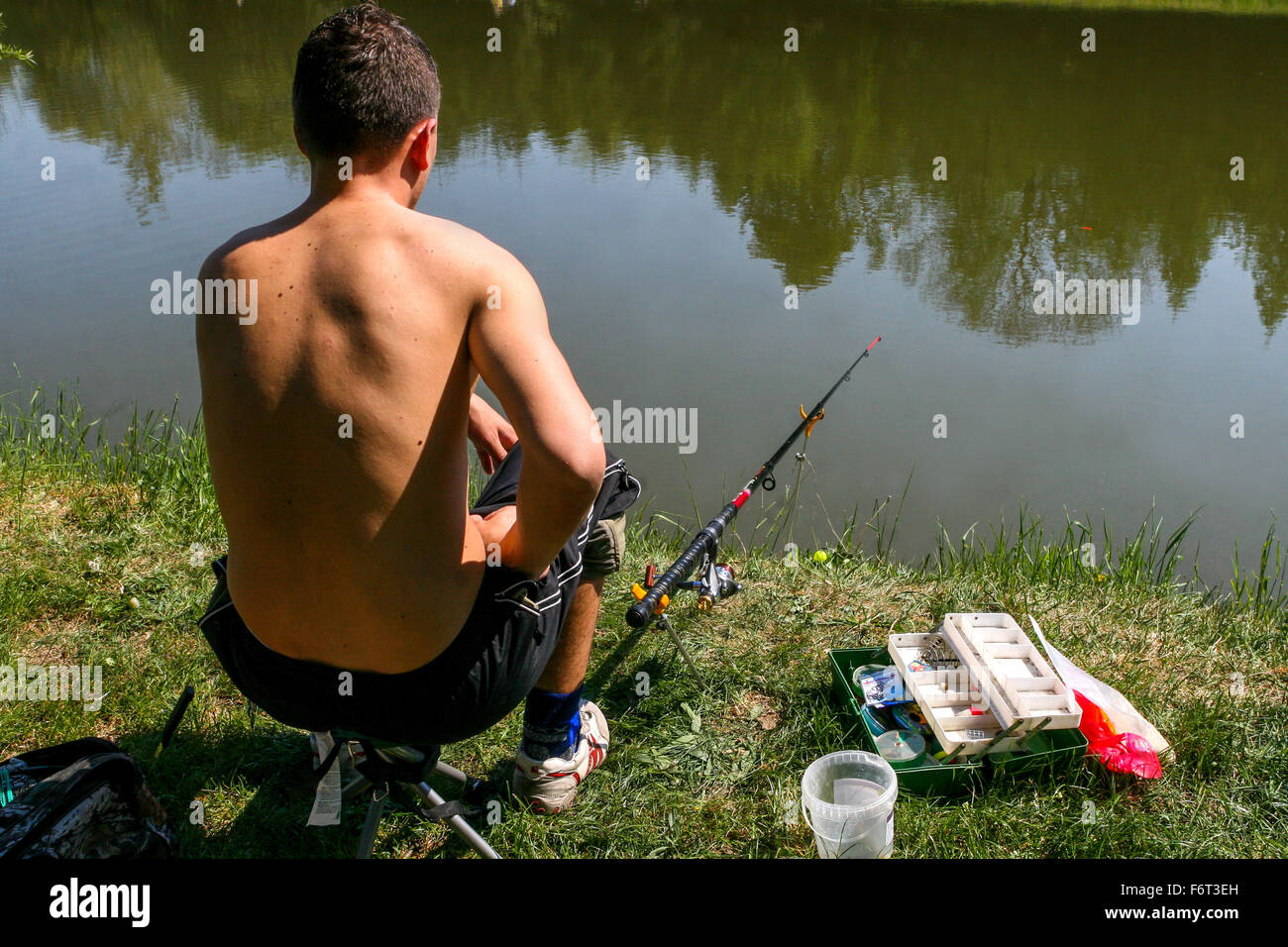 L'uomo seduto sulla riva pescato pesce, vista posteriore, canna da pesca, acqua sfondo, Foto Stock