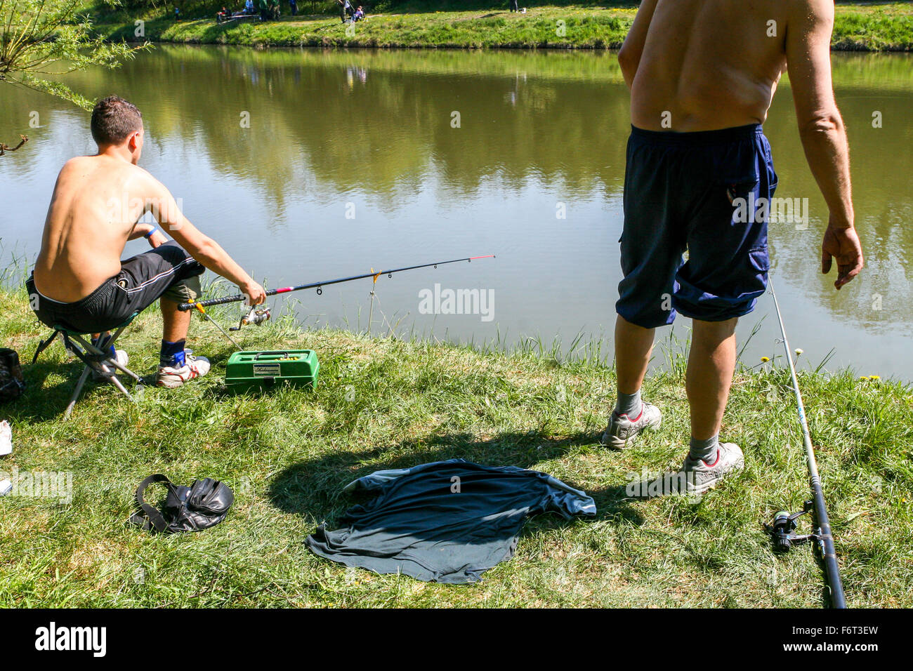 Due uomini sulla riva del fiume pescano pesce, canna da pesca, acqua sfondo Foto Stock
