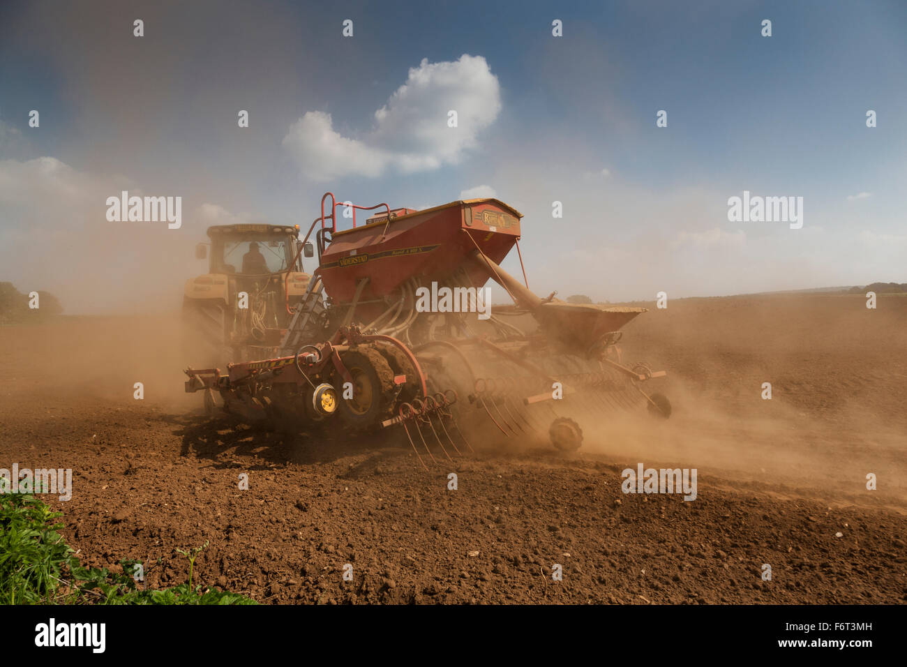 Il trattore genera polvere come si rimorchia un grande seminatrice dietro di essa mentre piantare il seme. Foto Stock