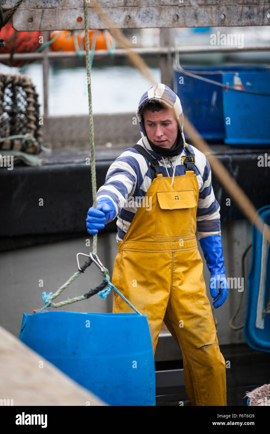 Un pescatore che indossa il giallo incerato guide una vasca contenente la cattura di crostacei su scalo nel porto di Dartmouth. Foto Stock