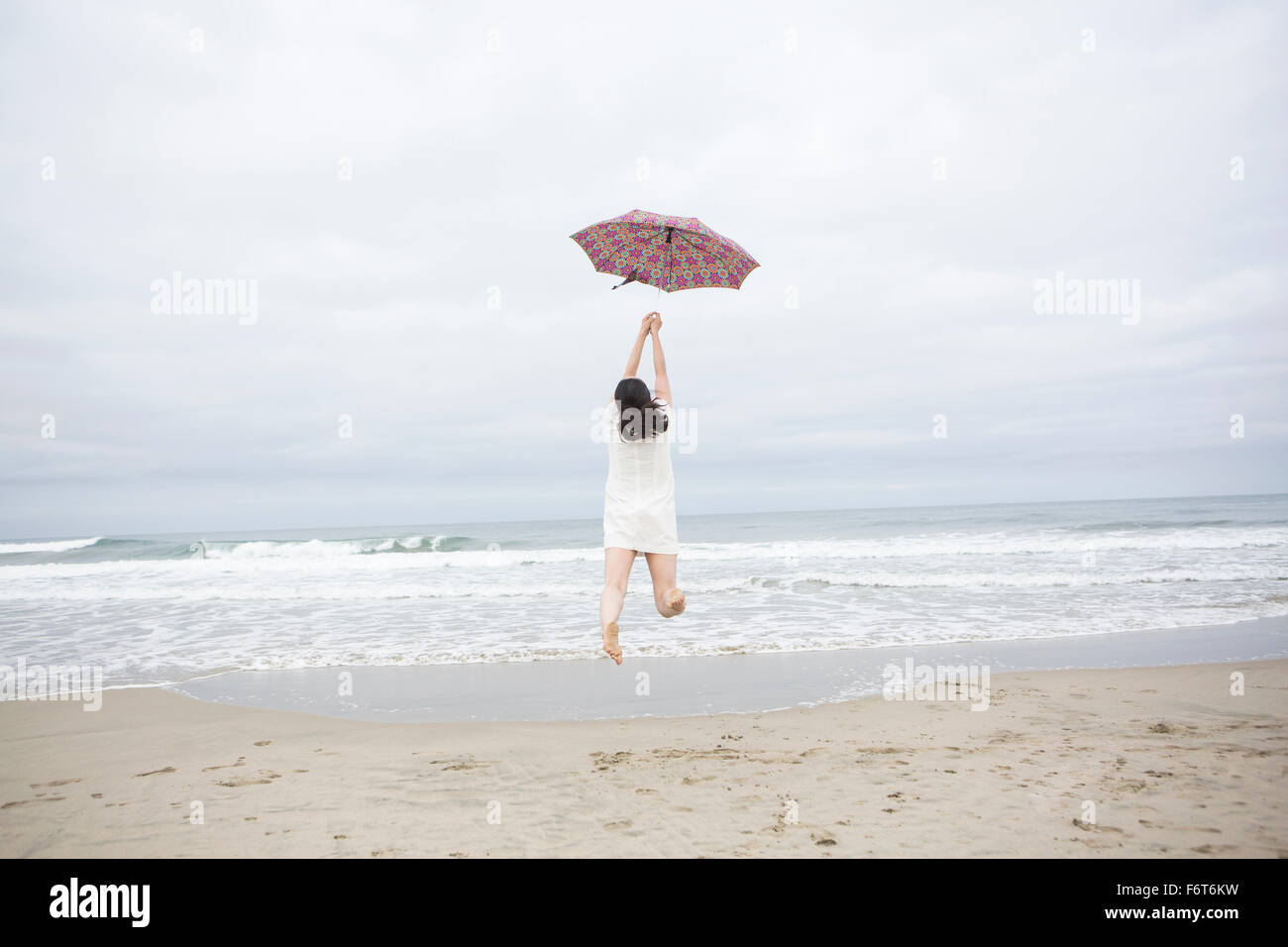 Donna che gioca con ombrellone in spiaggia Foto Stock